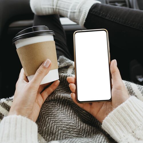 年轻前视图：一个拿着一个空白电话和一杯咖啡的女人冬天室内智能手机