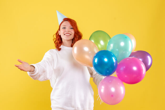 庆祝黄色墙壁上手持彩色气球的年轻女子的正视图年轻的女性女性年轻