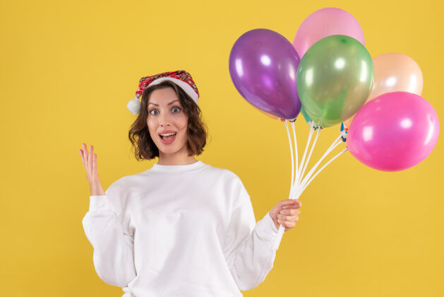 年轻的女性黄色墙壁上手持彩色气球的年轻女子的正视图气球前面庆祝