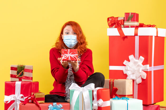 病毒坐在黄色墙壁上戴着面具的年轻女子的圣诞礼物前视图快乐前面面具