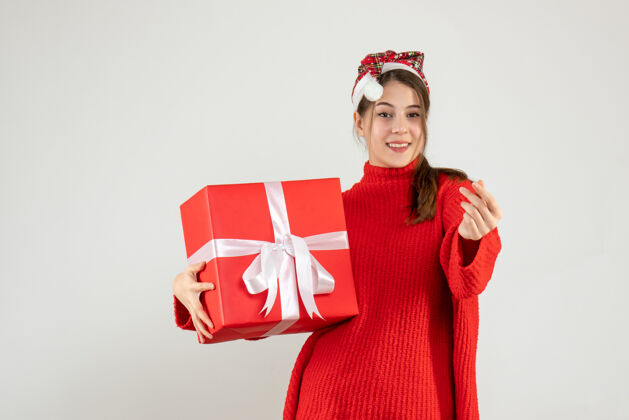 圣诞节戴着圣诞帽的快乐女孩拿着礼物站在白色的舞台上礼物服装快乐的女孩