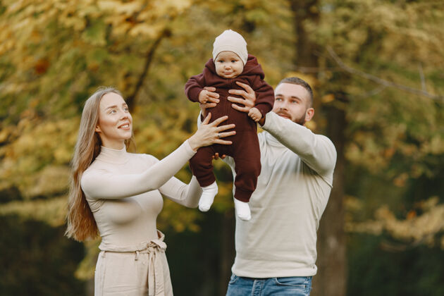 树叶秋天公园里的一家人穿棕色毛衣的男人和父母在一起的可爱小女孩黑发享受女儿