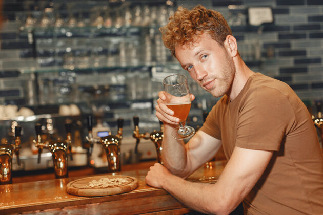 啤酒有魅力的年轻人站在吧台后面一个穿着棕色t恤的男人手里拿着一个玻璃杯酒吧醉酒顾客
