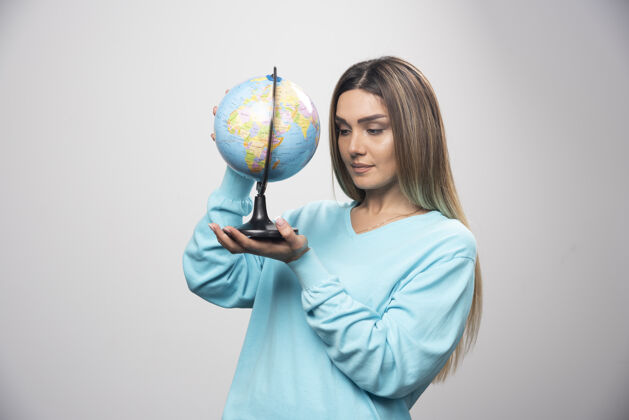 地球穿着蓝色运动衫的金发女孩手里拿着地球仪 仔细地查看着地球地图地理年轻人地点