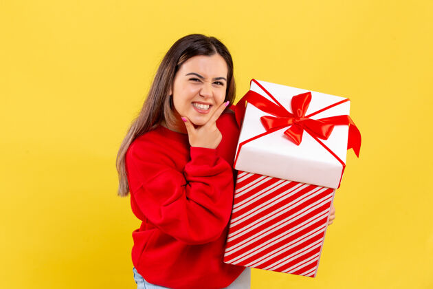 人黄色墙壁上 年轻女子拿着盒子里的圣诞礼物成人年轻十二月