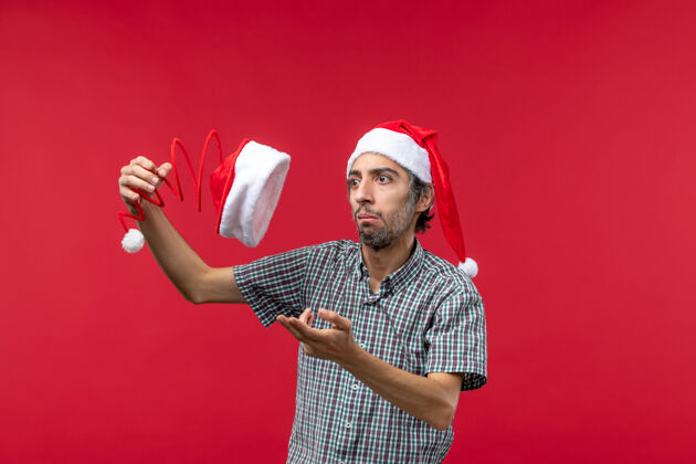 圣诞节前视图的年轻人举行圣诞玩具帽在红墙年轻男性肖像商业