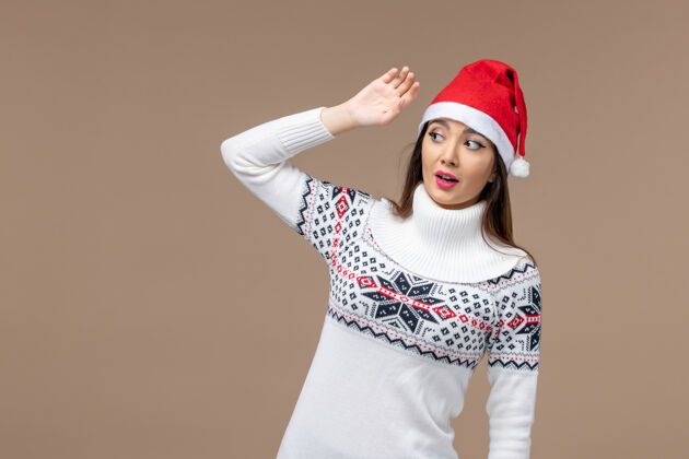 开朗正面图：棕色背景上戴着红色圣诞帽的年轻女性圣诞情绪肖像帽子风景
