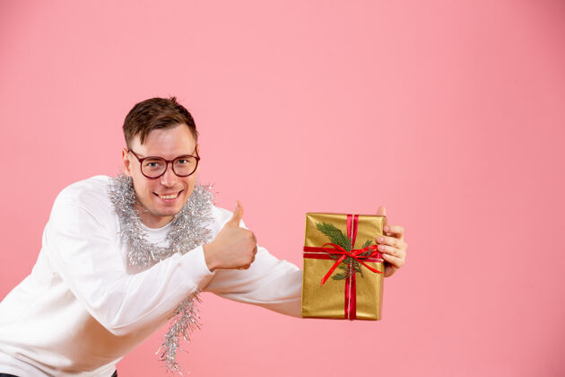男性粉红色墙上年轻人拿着圣诞礼物的正面图盒子微笑节日