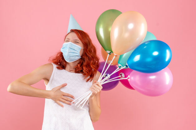年轻前视图中的年轻女子拿着五颜六色的气球在无菌面具上粉红色的墙壁面具无菌病毒