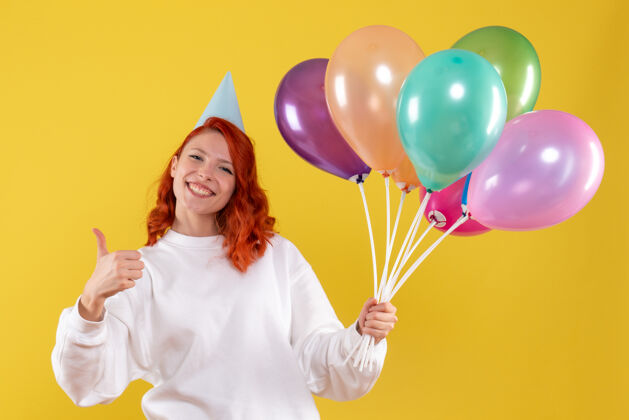 年轻前视图的年轻女子手持可爱的彩色气球在黄色的墙上圣诞节气球气球