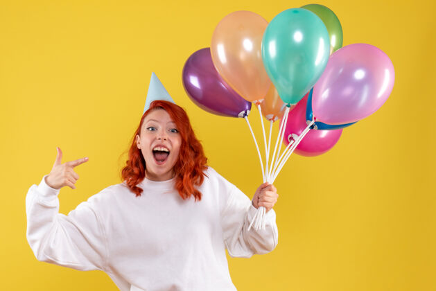 生日黄色墙壁上手持彩色气球的年轻女子的正视图年轻年轻的女性庆祝