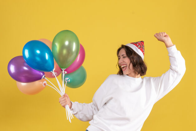 前面年轻女子手持五颜六色的气球在黄色墙壁上欢庆的正面图聚会庆祝生日