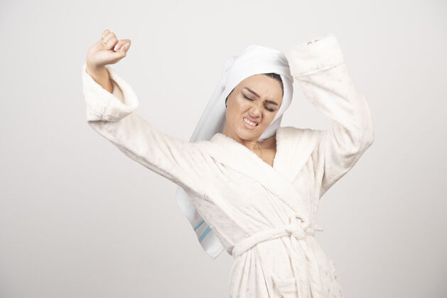 后穿着白色浴袍的漂亮年轻女子在白墙上摆姿势女性淋浴毛巾