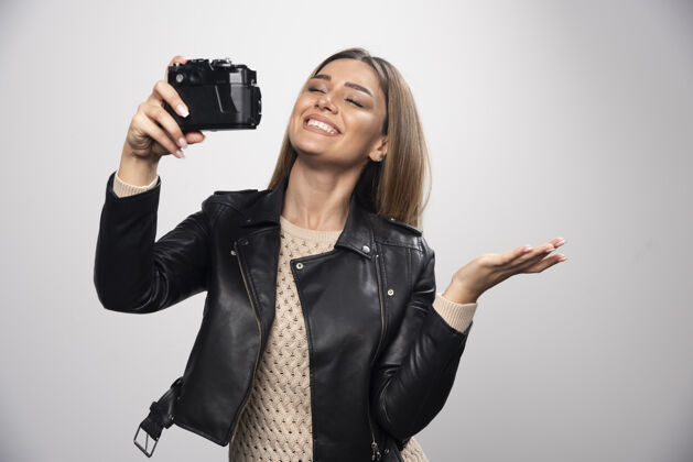 女人穿着黑色皮夹克的金发女孩拿着相机自拍数码单反女性摄影