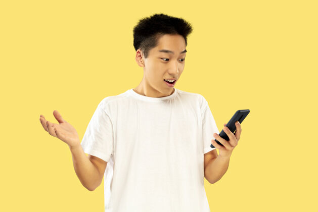 手势韩国年轻人的肖像穿白衬衫的男模使用智能手机下注 看新闻或聊天人类情感的概念 面部表情男人男人新闻