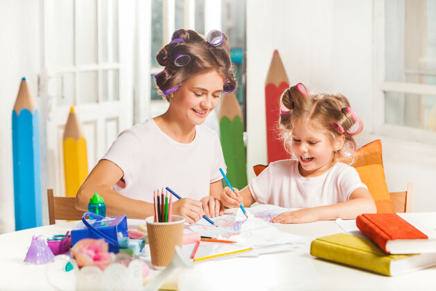教学年轻的母亲和她的小女儿在家里用铅笔画画绘画女儿妈妈