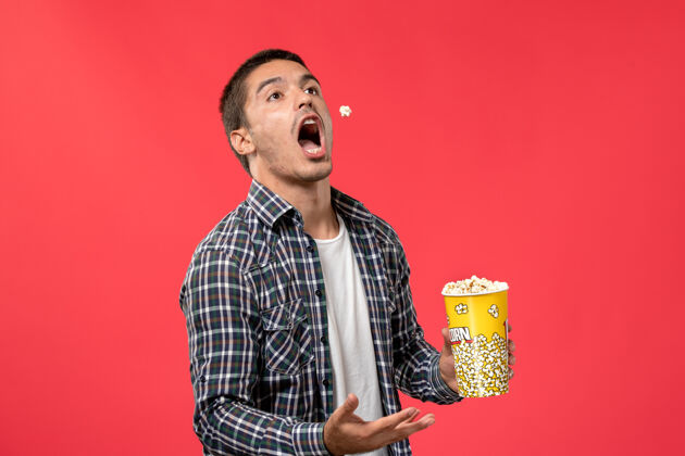 爆米花正面图：年轻男子拿着爆米花包站在红地板电影院里艺人观点歌手