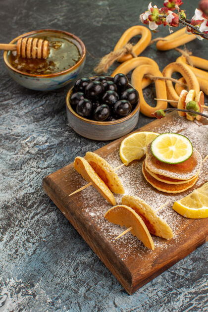 桌子水果煎饼的垂直视图靠近蜂蜜的饼干在碗里 黑色的樱桃在灰色的桌子上蜂蜜美食水果煎饼