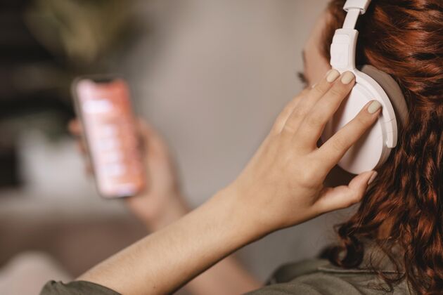 女性在家沙发上用现代智能手机和耳机的女人科技小玩意年轻人