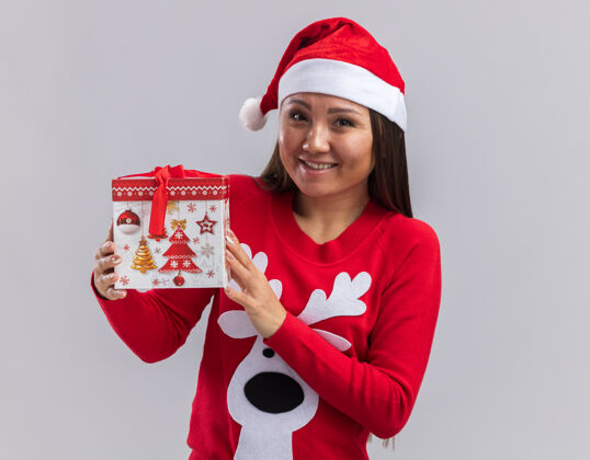 圣诞节笑容满面的年轻亚洲女孩戴着圣诞帽 拿着一个白色背景的礼品盒帽子毛衣女孩