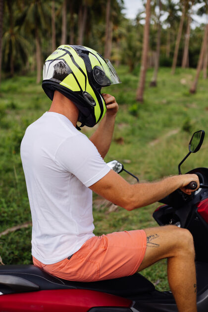 滑板车戴着太阳镜 戴着头盔 穿着蓝色敞篷衬衫骑着摩托车的时尚纹身男游客的肖像车辆引擎轮子