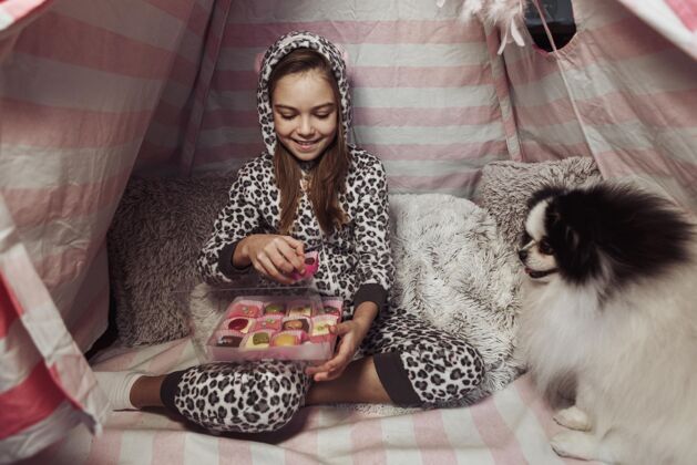 快乐在室内帐篷和狗里吃糖果的女孩宠物小狗孩子