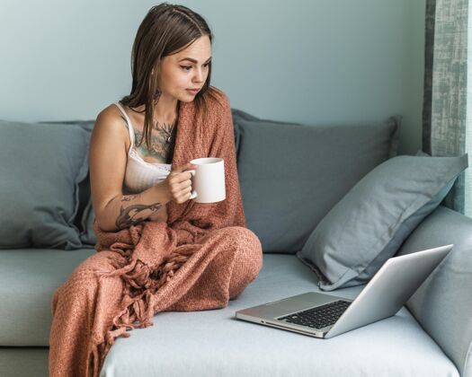 防护在流感大流行期间 一个穿着毯子在家里喝咖啡和用笔记本电脑工作的女人复制女性杯子