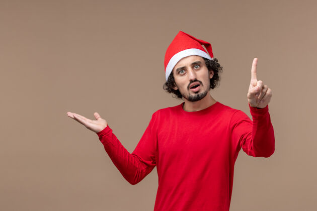 服装正面图：年轻人在圣诞节的棕色背景上带着惊讶的表情年轻人男性帽子