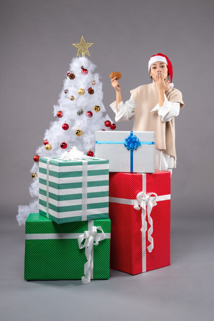 礼物在圣诞树旁的灰色地板上 年轻的女人拿着饼干和礼物年轻圣诞树圣诞树