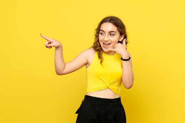 年轻女性黄墙上年轻女子模仿电话的正面图年轻女性生活方式