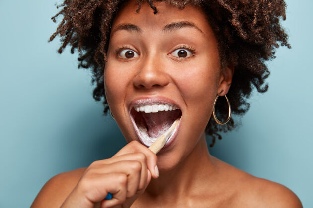 卫生牙齿护理 美丽和快乐的概念积极的非裔美国少女张大嘴巴 早上用牙刷和牙膏刷牙 感觉快乐 模型在蓝色的墙壁上快乐女人非洲