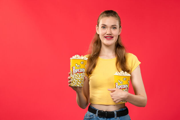 女正面图年轻女性在电影院拿着爆米花 微笑着看红墙电影院的女性趣味电影漂亮黑发年轻