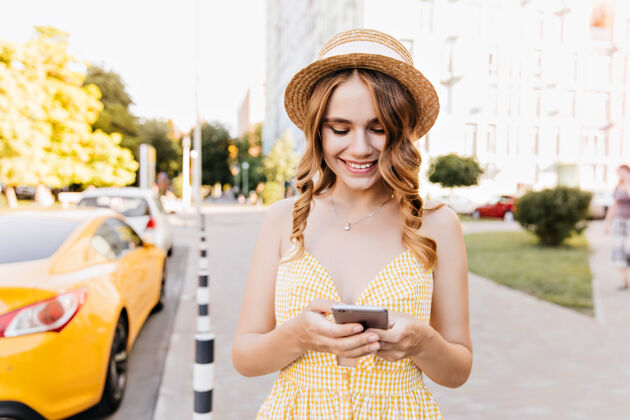智能手机可爱迷人的女孩站在街上发短信穿着复古帽子和智能手机合影的可爱女人的户外肖像城市景观休息帽子