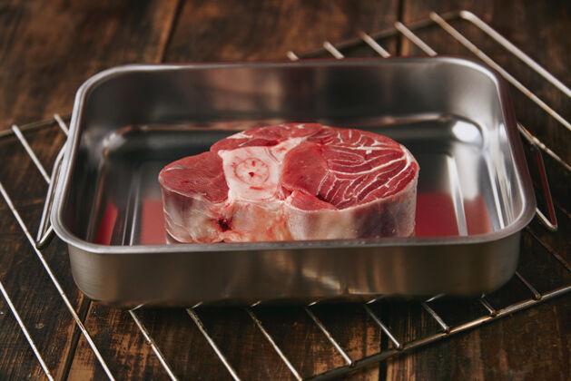 桌子原汁原味的安格斯腿牛排放在木制桌子上的银色铁锅里 红色背景食肉动物木头农场