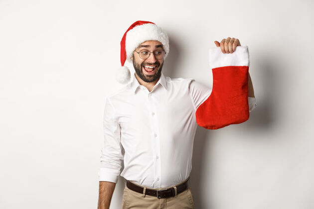 圣诞节圣诞快乐 节日概念快乐的成年人收到礼物在圣诞节袜子 看起来很兴奋 戴着圣诞帽脸微笑西装