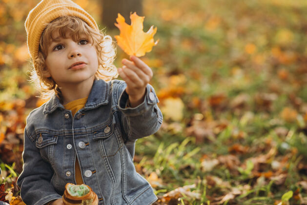 森林可爱的小男孩在公园吃羊角面包瞬间玩秋天