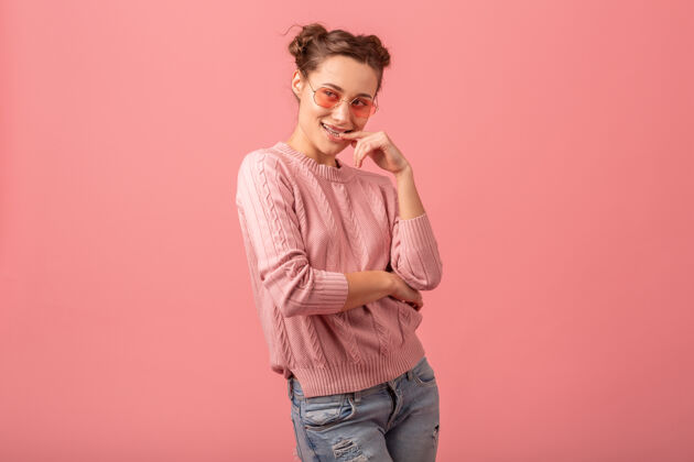 女性年轻漂亮的微笑调情女子在粉红色的毛衣和太阳镜孤立在粉红色的工作室背景粉色眼镜脸