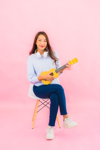年轻肖像美丽的亚洲年轻女子在粉红色的隔离墙上演奏四弦琴可爱的女孩演奏女人