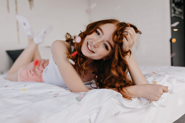 人顽皮的姜黄色女模特在床上摆出真诚的微笑室内拍摄的温文尔雅的高加索女孩在卧室里大笑年轻醒室内