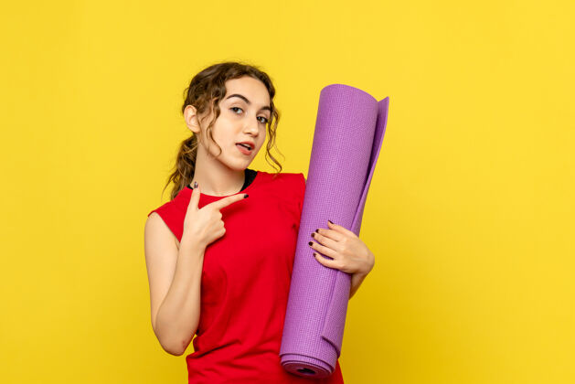 女人黄色墙壁上拿着紫色地毯的年轻女子的正视图地毯设备年轻女性