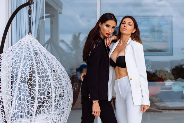 服装两个穿着黑白西装的时髦女人站在别墅外的玻璃墙上奢侈品成功商业
