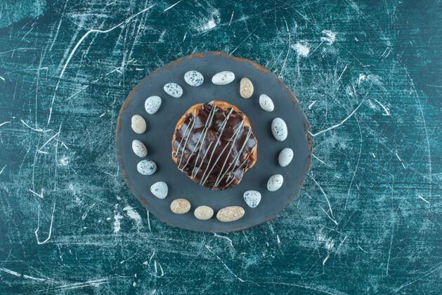 点心在蓝色的木板上 巧克力蛋糕周围环绕着糖果块糖顶部视图美味
