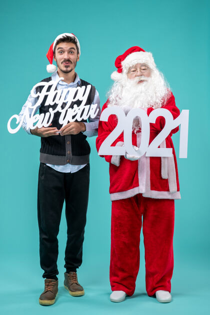 快乐圣诞老人的正面图 蓝色墙壁上有人拿着新年快乐和2021年的木板人男人商务