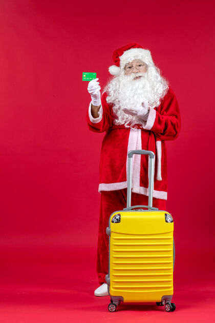 服装红墙上挂着黄色袋子 手里拿着绿色银行卡的圣诞老人的正视图快乐圣诞圣诞快乐