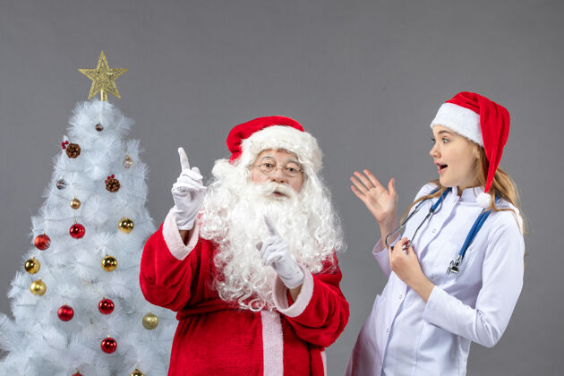 年轻圣诞老人和年轻女医生在灰色墙上的正视图女性圣诞人们