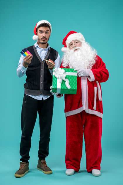 圣诞圣诞老人与年轻人和节日礼物在蓝色墙上的正面视图节日套装庆祝