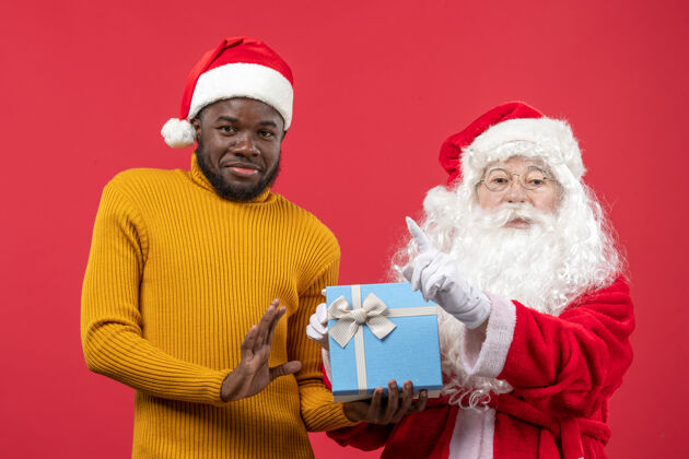 圣诞老人红墙上的圣诞老人和拿着礼物的年轻人的正视图十二月举行肖像