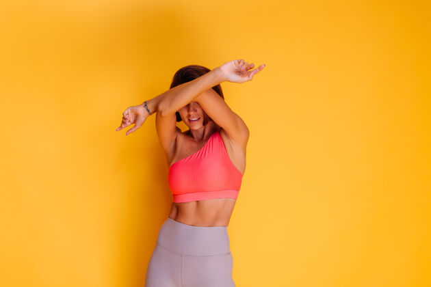 锻炼年轻健壮的女人穿着运动服 时髦的上衣和紧身裤 对着黄色的墙壁摆姿势腹部臀部成人