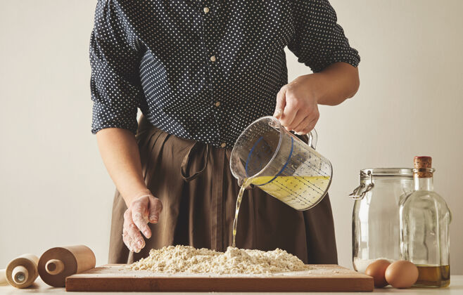 手工制作女人把水和橄榄油从量杯倒到面粉上 准备面团或饺子烹饪指南介绍意大利馄饨意大利