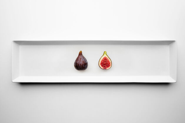 异国情调两个成熟的新鲜无花果隔离在中心矩形陶瓷板上的白色桌子部分切片种子